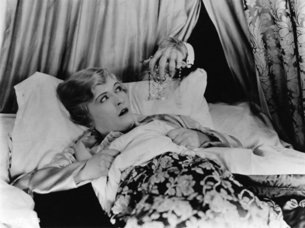 A blonde woman is lying in bed, looking distressed. From behind, the hairy claw of a monster reaches for her
