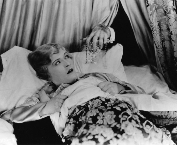 A blonde woman is lying in bed, looking distressed. From behind, the hairy claw of a monster reaches for her