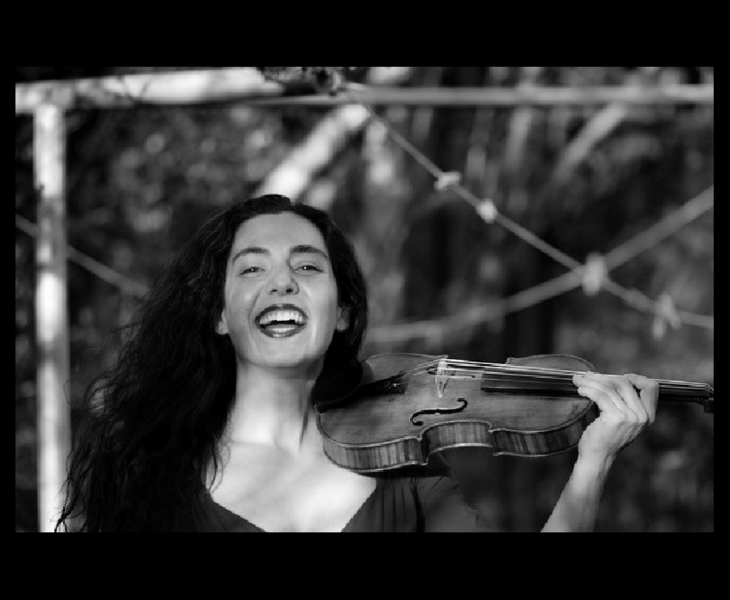 A laughing woman with long dark hair holding a violin