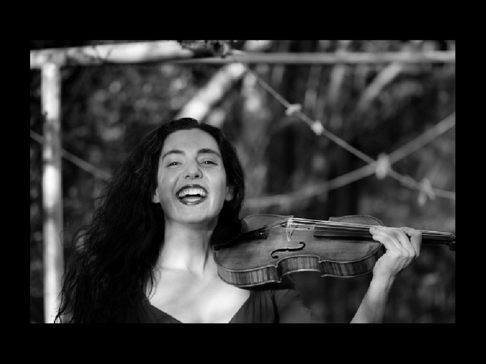 A laughing woman with long dark hair holding a violin
